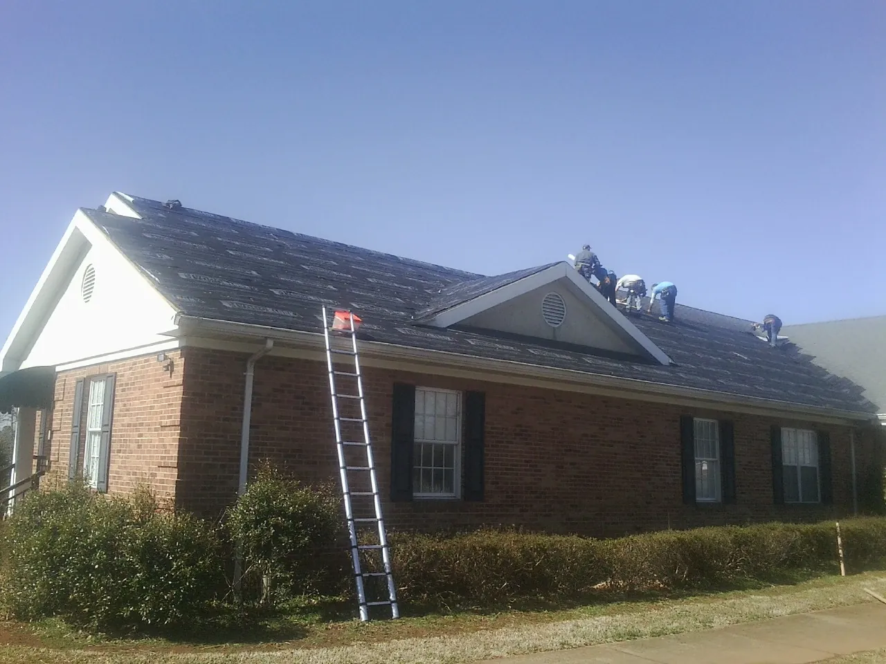 Crew tearing shingles off a brick ranch roof with a ladder set — Emergency Roof Repair work by our crew in Chelsea