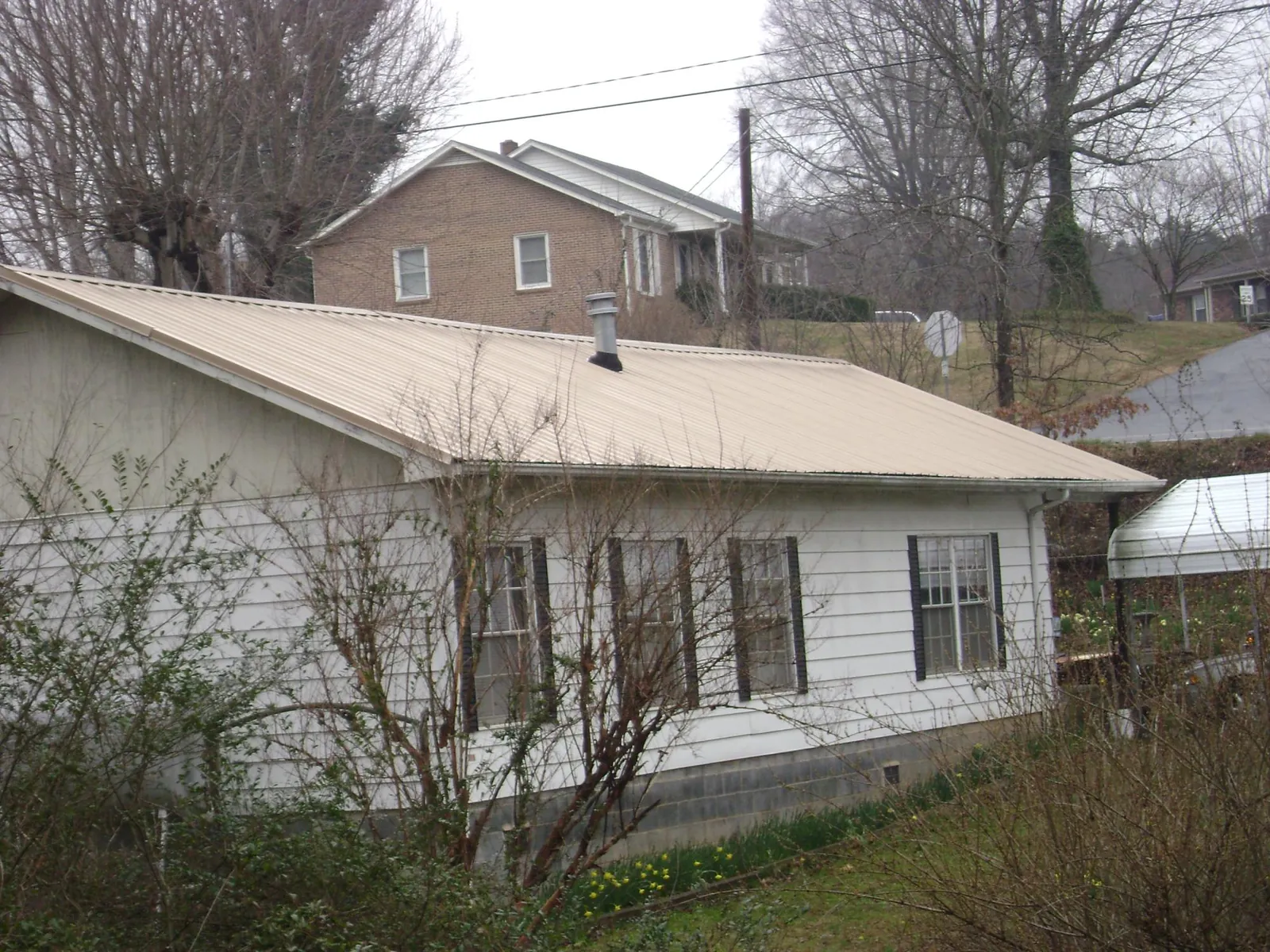 Tan metal roof on a white sided house set into a hillside — Commercial Roofing by Roofing Brothers in Chelsea
